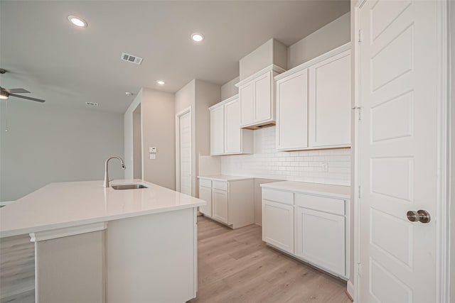 kitchen with backsplash, light wood-style floors, a center island with sink, ceiling fan, and a sink