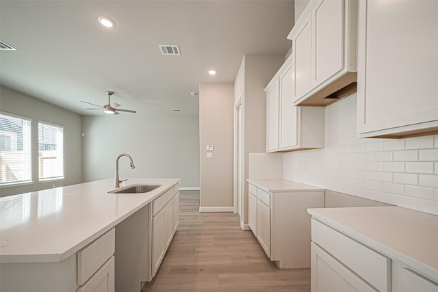 kitchen featuring visible vents, a sink, ceiling fan, light wood-type flooring, and backsplash