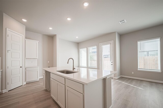 kitchen with white cabinets, light wood-style floors, a sink, and visible vents