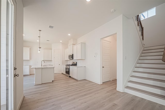 kitchen featuring a center island with sink, visible vents, light wood-style flooring, and appliances with stainless steel finishes