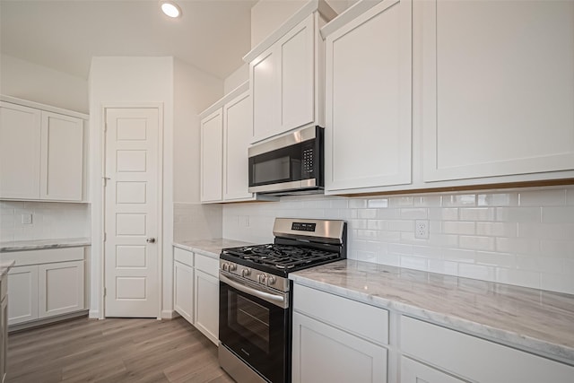 kitchen featuring white cabinetry, light stone counters, stainless steel appliances, light wood finished floors, and backsplash