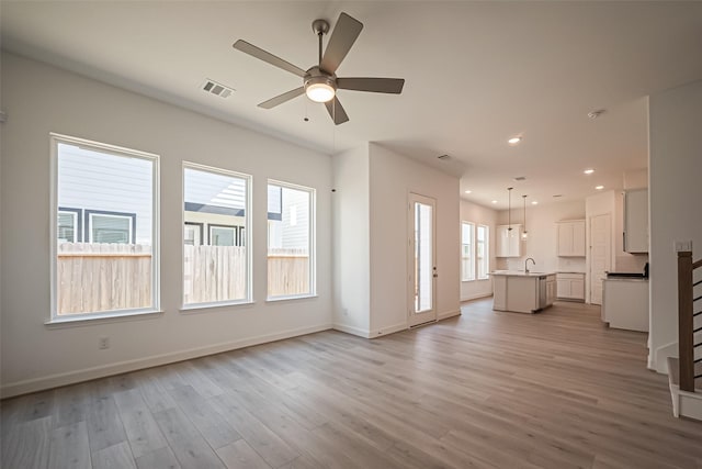 unfurnished living room featuring visible vents, baseboards, a sink, ceiling fan, and light wood-style floors