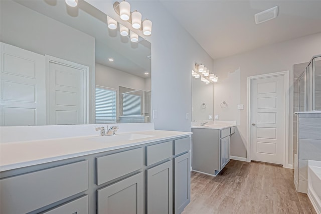 full bath with visible vents, a sink, a shower stall, wood finished floors, and two vanities