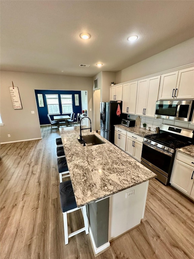 31503 Sandpiper Creek Dr, Hockley, TX 77447 - kitchen with appliances with stainless steel finishes, a sink, light wood finished floors, white cabinetry, and recessed lighting