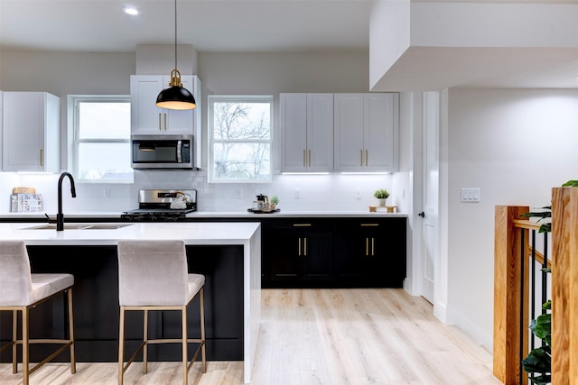 kitchen featuring appliances with stainless steel finishes, light countertops, dark cabinetry, a healthy amount of sunlight, and a sink