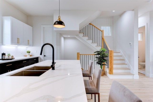 kitchen featuring hanging light fixtures, a sink, dark cabinetry, light stone countertops, and light wood-style flooring