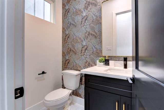 half bath with toilet, baseboards, vanity, and wallpapered walls