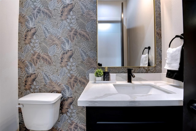 half bathroom with toilet, vanity, and wallpapered walls