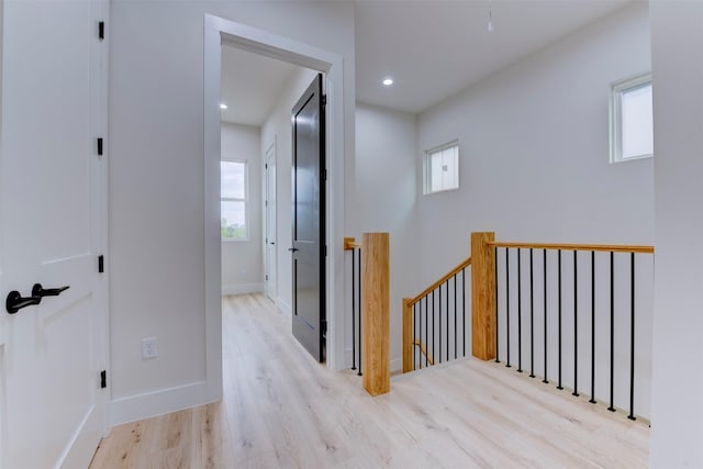 hallway with a wealth of natural light, an upstairs landing, wood finished floors, and baseboards