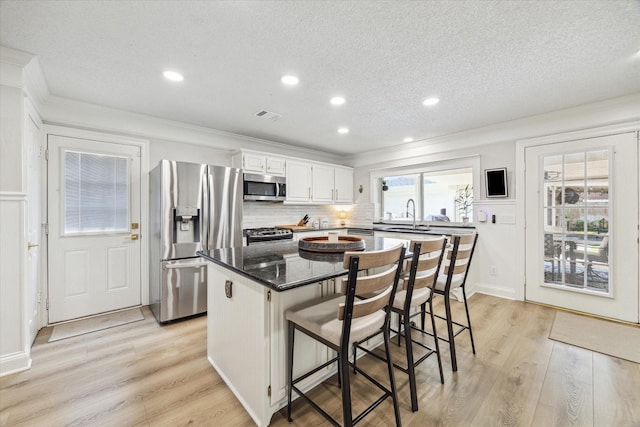 kitchen with white cabinets, a kitchen island, crown molding, light wood-style flooring, and appliances with stainless steel finishes