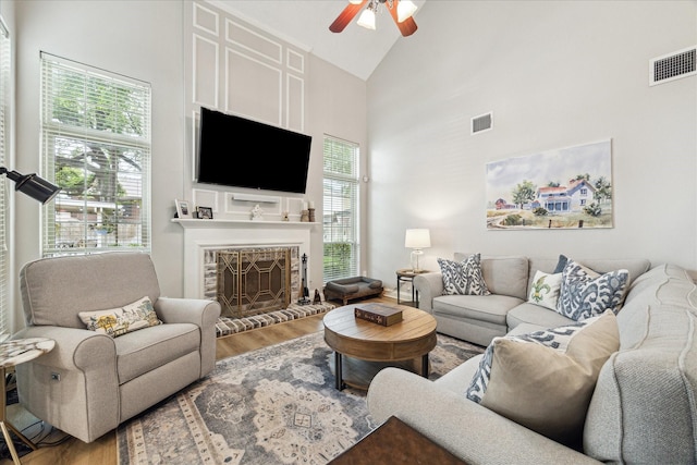 living room with visible vents, a ceiling fan, wood finished floors, a brick fireplace, and high vaulted ceiling
