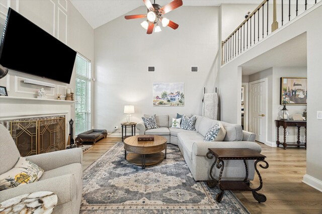 living area with wood finished floors, visible vents, baseboards, high vaulted ceiling, and ceiling fan