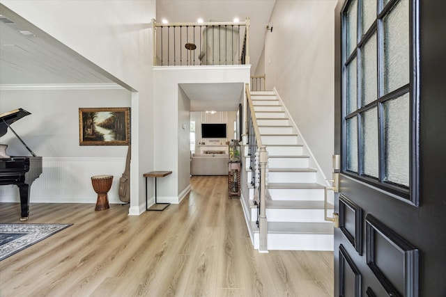 entryway with baseboards, wood finished floors, a high ceiling, stairs, and crown molding