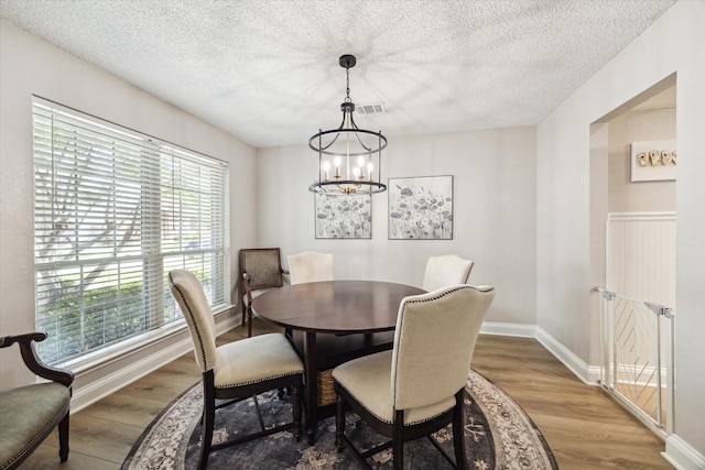 dining space featuring wood finished floors, an inviting chandelier, and a textured ceiling