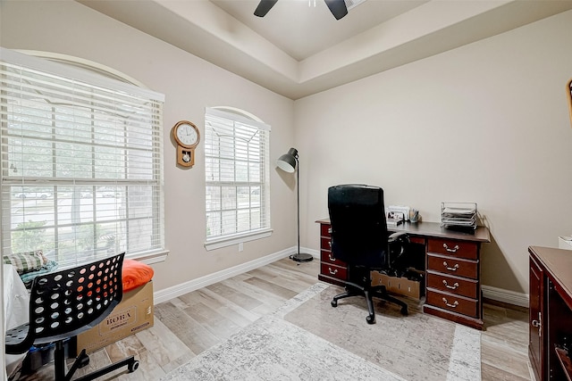 office area featuring a tray ceiling, light wood finished floors, baseboards, and a ceiling fan