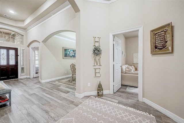 entryway featuring arched walkways, a high ceiling, wood finished floors, and ornamental molding