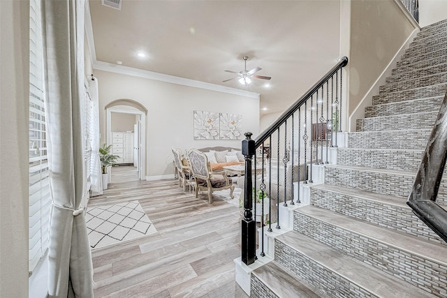 entrance foyer with arched walkways, stairs, crown molding, and a ceiling fan