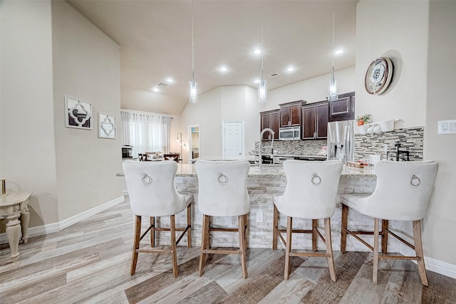 kitchen with dark brown cabinetry, light wood-style flooring, recessed lighting, a breakfast bar, and appliances with stainless steel finishes