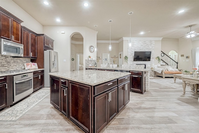 kitchen with open floor plan, a ceiling fan, a kitchen island, stainless steel appliances, and arched walkways