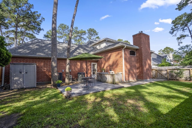 back of house featuring a gate, a chimney, brick siding, a yard, and a patio
