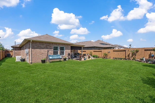 rear view of house with brick siding, central air condition unit, a lawn, and a fenced backyard