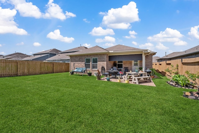 rear view of property featuring brick siding, a yard, a patio area, and a fenced backyard