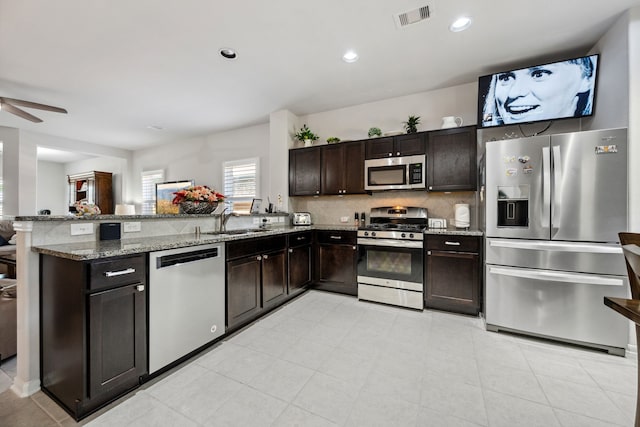 kitchen featuring a peninsula, visible vents, decorative backsplash, light stone counters, and appliances with stainless steel finishes