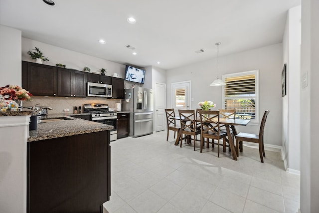 kitchen featuring dark stone countertops, a sink, dark brown cabinetry, stainless steel appliances, and backsplash