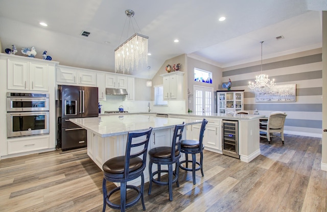 kitchen with an inviting chandelier, a peninsula, under cabinet range hood, appliances with stainless steel finishes, and beverage cooler