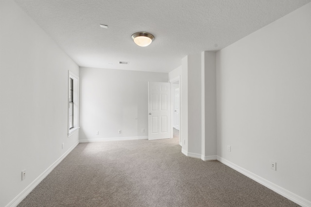 carpeted spare room featuring visible vents, baseboards, and a textured ceiling