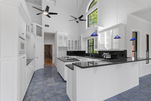 kitchen featuring glass insert cabinets, a peninsula, a ceiling fan, visible vents, and a sink