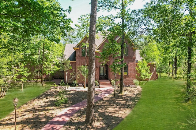 tudor-style house with brick siding, a front yard, and roof with shingles