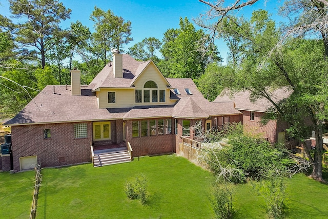 rear view of property featuring an attached garage, a chimney, brick siding, and a yard