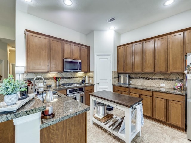 kitchen with a peninsula, backsplash, visible vents, appliances with stainless steel finishes, and a sink