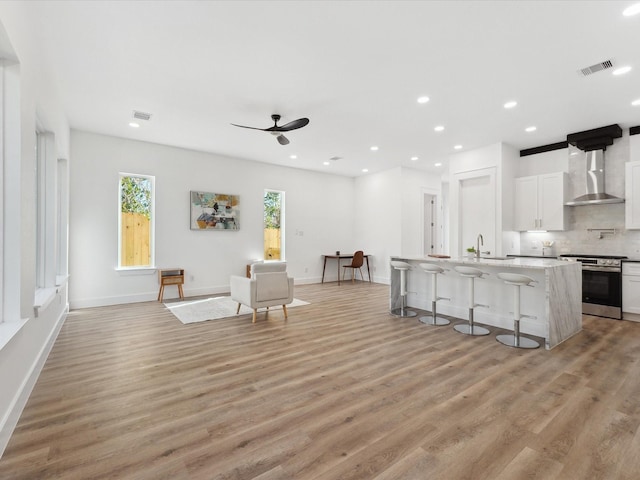 kitchen featuring light wood-type flooring, wall chimney range hood, electric range, visible vents, and a kitchen bar