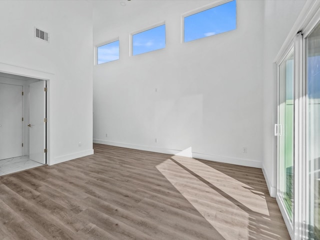 unfurnished living room with visible vents, baseboards, a high ceiling, and wood finished floors