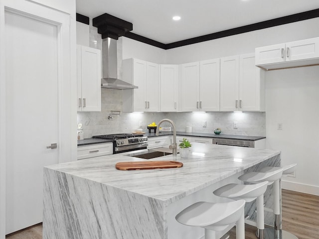 kitchen featuring light wood-style floors, stainless steel range with gas cooktop, wall chimney exhaust hood, white cabinets, and decorative backsplash