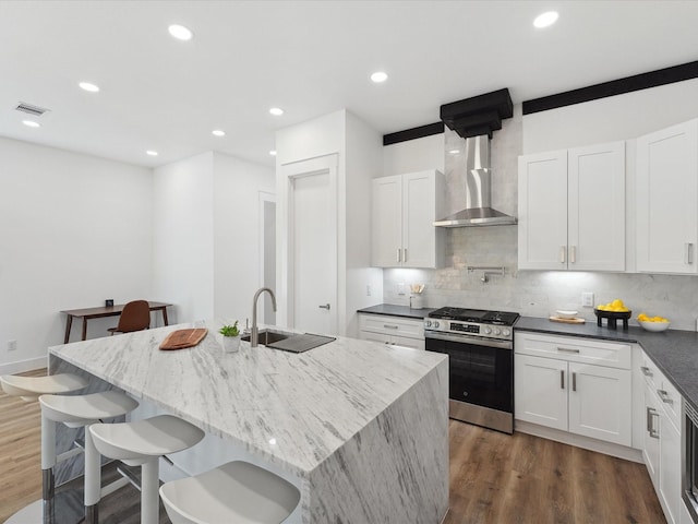 kitchen with wall chimney range hood, stainless steel gas range, dark wood-style flooring, and a sink