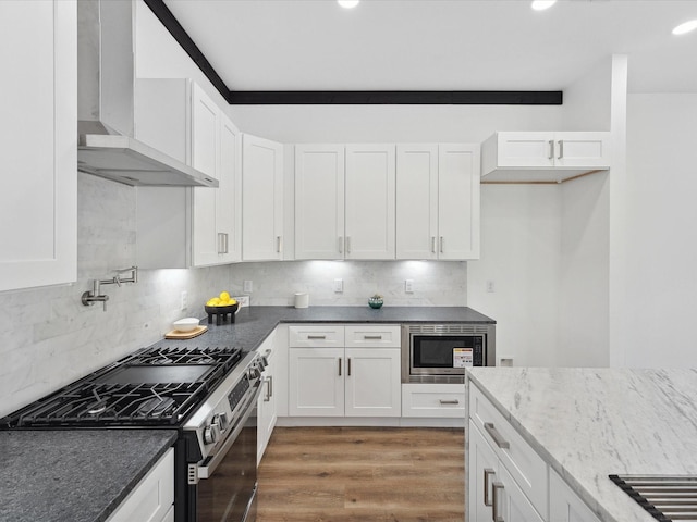 kitchen featuring dark stone countertops, wall chimney range hood, white cabinetry, and stainless steel appliances