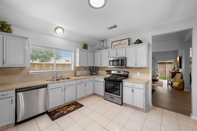 kitchen featuring appliances with stainless steel finishes, a wealth of natural light, visible vents, lofted ceiling, and a sink