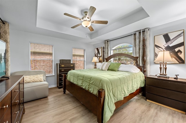 bedroom featuring a tray ceiling, ceiling fan, light wood finished floors, and baseboards