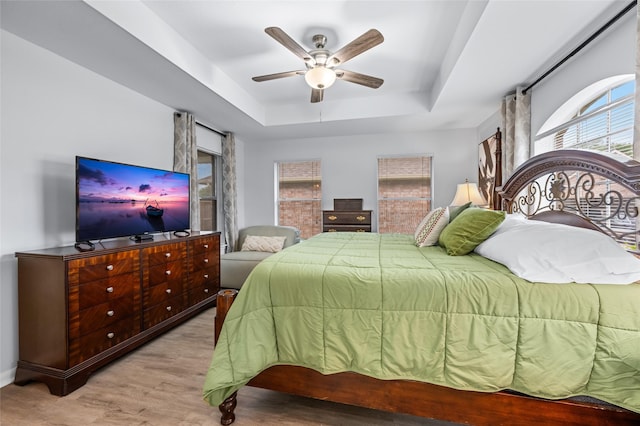 bedroom with multiple windows, a tray ceiling, a ceiling fan, and wood finished floors