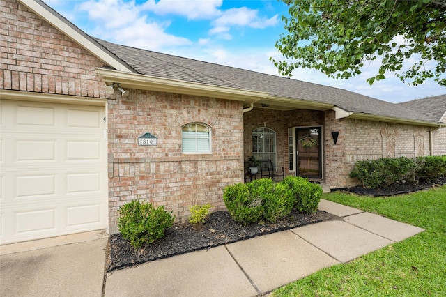 doorway to property with a shingled roof, a garage, and brick siding