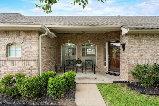 doorway to property featuring a shingled roof and brick siding