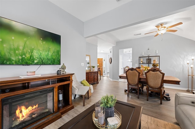 living area featuring a ceiling fan, vaulted ceiling, a glass covered fireplace, and light wood-style floors