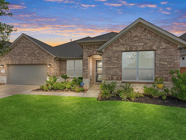 ranch-style home featuring a garage, a lawn, brick siding, a shingled roof, and concrete driveway