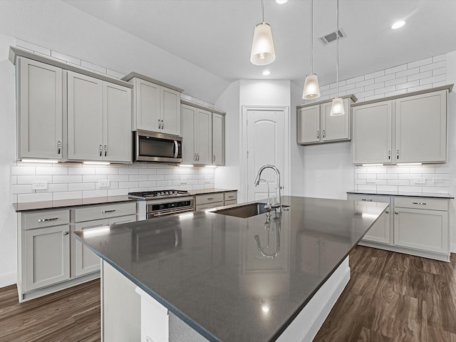 kitchen with visible vents, a sink, appliances with stainless steel finishes, dark countertops, and dark wood-style floors