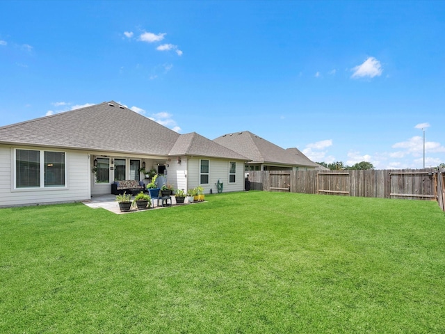 back of house with a shingled roof, a yard, a fenced backyard, and a patio area