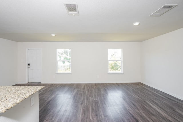 unfurnished room featuring dark wood-type flooring, visible vents, and plenty of natural light