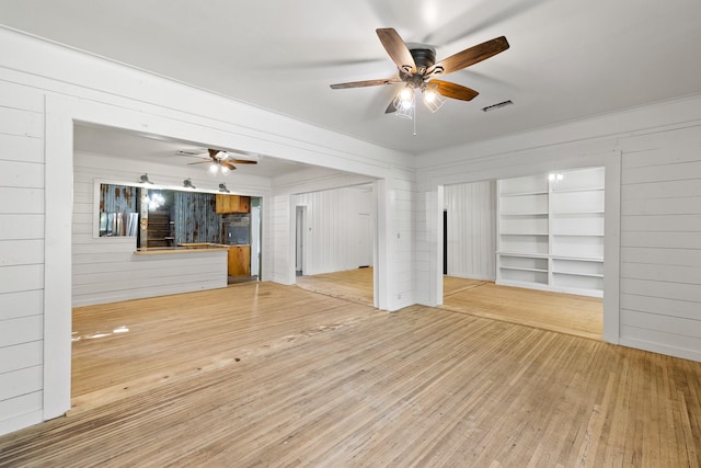 unfurnished living room featuring wood walls, a ceiling fan, visible vents, and hardwood / wood-style flooring